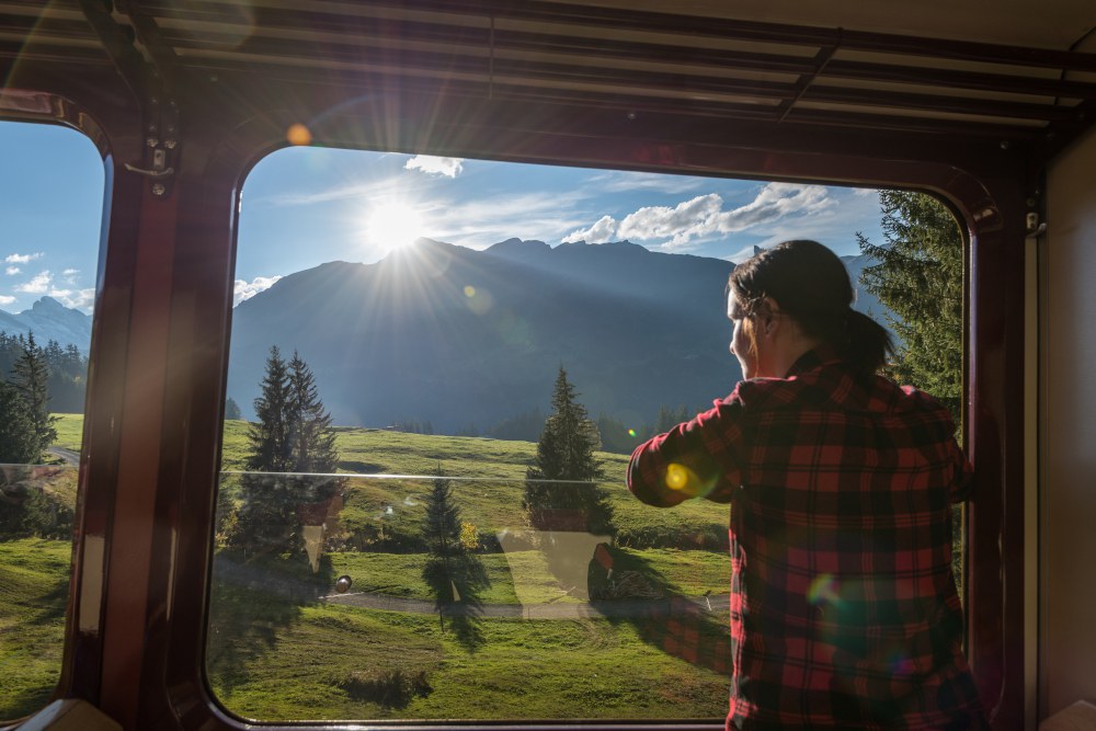 Junge Frau schaut aus dem Zugfenster auf die Berge.